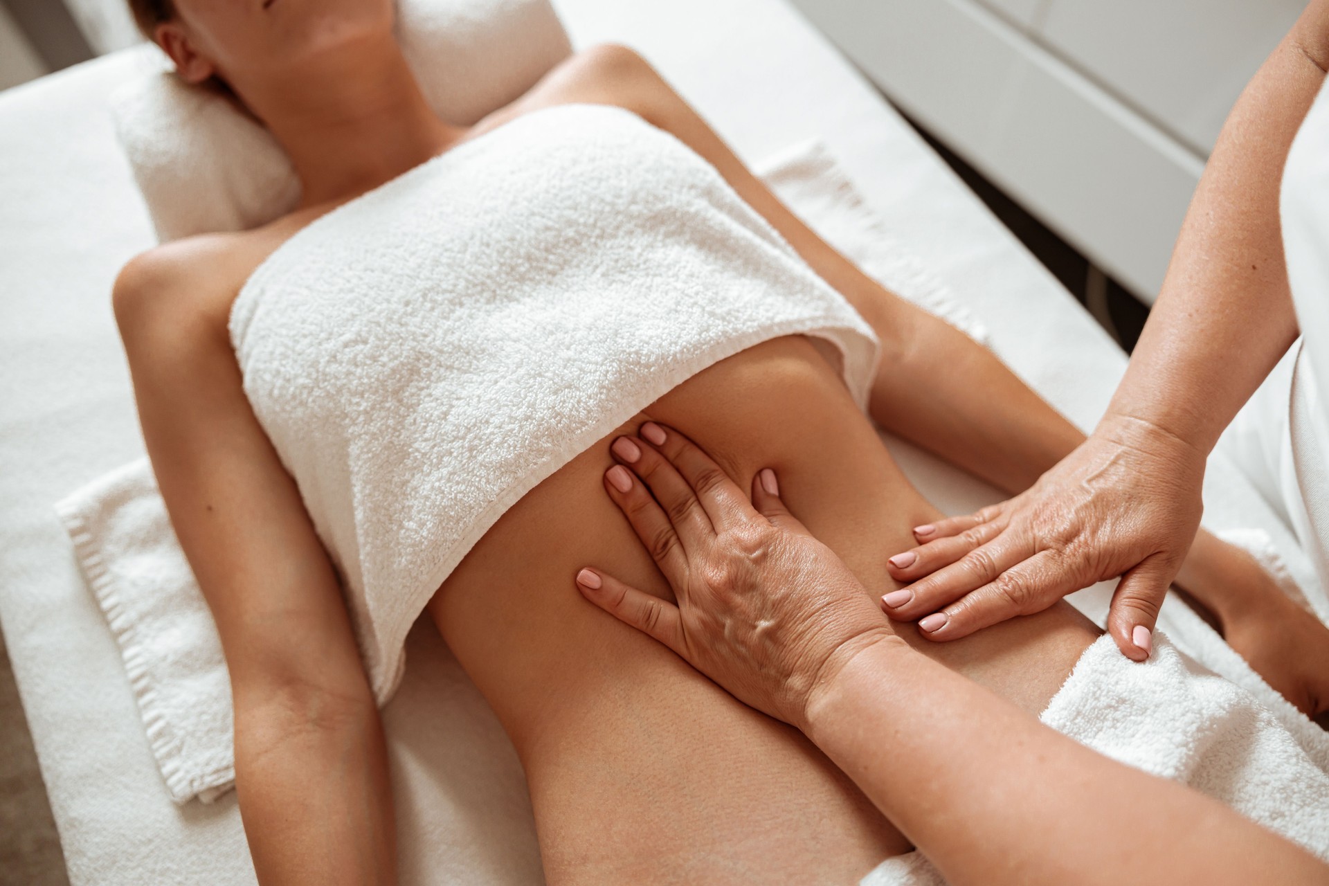 Masseuse massaging female client abdomen at wellness center
