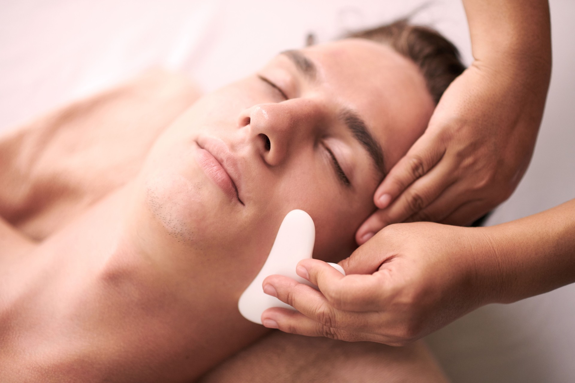 Young relaxed male client of spa salon getting luxurious facial massage